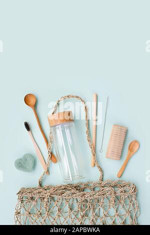 Natural accessories: luffa washcloth, bamboo toothbrush, glass drink bottle with bamboo cover, bamboo straw with metal brush, wooden comb and spoon in wicker shopping bag. Stock Photo