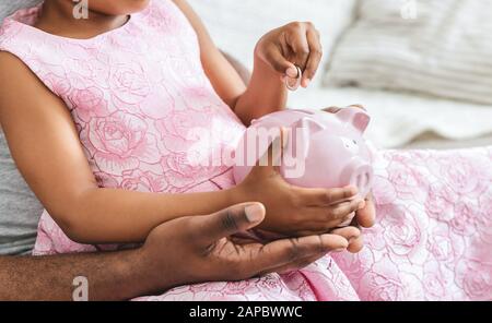 Cropped of black girl putting money in piggy bank Stock Photo