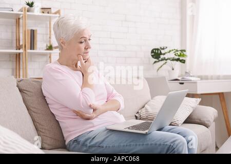 Puzzled senior lady looking at laptop with perplexity Stock Photo