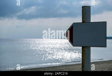 White empty , blank metal sign on rusty pole shows the direction to the sea. Sunbeams through clouds make sea's surface glittering. Blur background, c Stock Photo