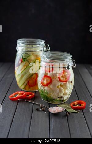 glass jars of fermented cauliflower, cucumbers, carrots, chili pepper, spices, salt. vegetables on a dark background. fermentation is a source of prob Stock Photo