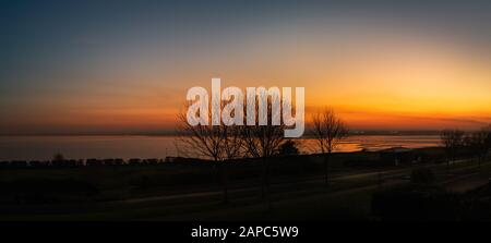 The silhouette of trees along the promenade of the west cliff in Ramsgate during a glorious sunset creating golden reflections in Pegwell Bay. Stock Photo