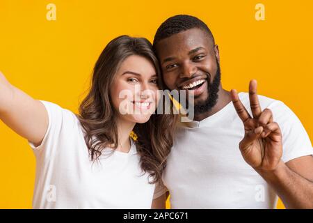Cheerful interrational couple taking selfie together, looking at camera and smiling Stock Photo