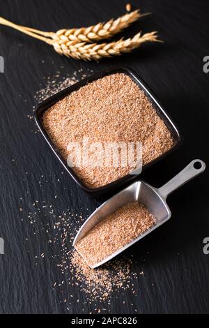 Healthy food concept Organic Wheat bran in black ceramic cup with wheat ear on black slate stone background Stock Photo