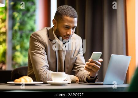 Portrait of busy afro guy using cellphone and computer Stock Photo