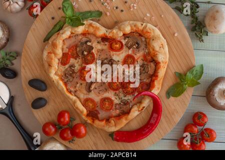 Pizza heart shaped with ham tomatoes and mushrooms on wooden background . Concept of romantic love for Valentines Day . Love food Stock Photo