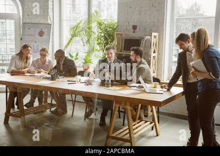 Concentrated. Group of young business professionals having a meeting. Diverse group of coworkers discuss new decisions, plans, results, strategy. Creativity, workplace, business, finance, teamwork. Stock Photo