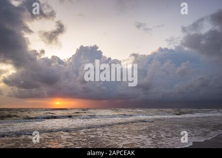 Sun sets over the sea below dramatic storm clouds Stock Photo