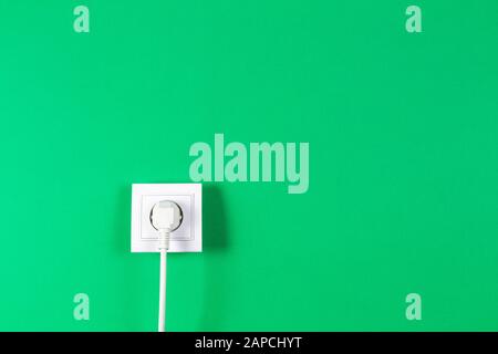 White cable plugged into electrical socket on green color background Stock Photo