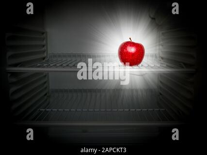 Conceptual creative photo of a glowing in the dark fresh red apple in an open empty refrigerator. Weight loss diet concept. Stock Photo