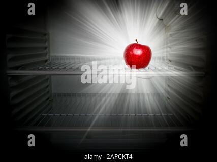 Conceptual creative photo of a glowing in the dark fresh red apple in an open empty refrigerator. Weight loss diet concept. Stock Photo