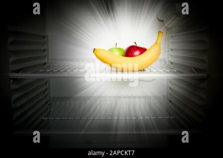 Conceptual creative photo of fresh red and green apples and banana glowing in the dark in an open empty refrigerator. Weight loss diet concept. Stock Photo