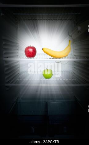 Conceptual creative photo of fresh red and green apples and banana glowing in the dark in an open empty refrigerator. Weight loss diet concept. Stock Photo