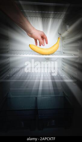 A man's hand reaches out for a single banana glowing in the dark in an open empty refrigerator. Weight loss diet concept. Stock Photo