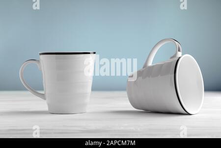 Two blank white mugs on white table and blue background. White blank mugs mock up. Stock Photo