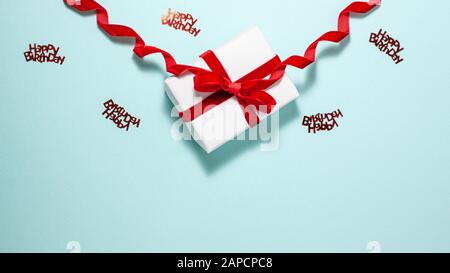White gift box with a red velvet ribbon bow and happy bithday sign at the top on blue background. Flat lay top view. Gift and holidays concept with co Stock Photo