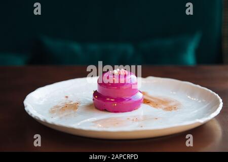 Round cake with walnut filling poured pink glaze. On a white plate, standing on the table. Stock Photo