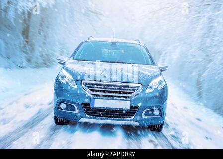 Car drives through the snow. Winter driving concept. Road and trees in motion. Front view of the car on the road Stock Photo