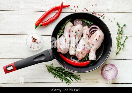 Raw marinated chicken legs or drumsticks with spices and herbs in a frying pan ready for cooking. Mediterranean food concept. Top view Stock Photo