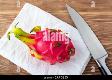 Whole dragon fruit or pitaya on a white linen napkin over brown wooden table. Fruits and vegetables. Healthy vegetarian food rich in B vitamins. Stock Photo
