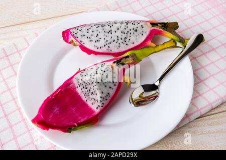 Two parts of dragon fruit or pitaya and spoon on a plate over a white wooden table. Healthy vegetarian food rich in B vitamins and tannin. Front view. Stock Photo