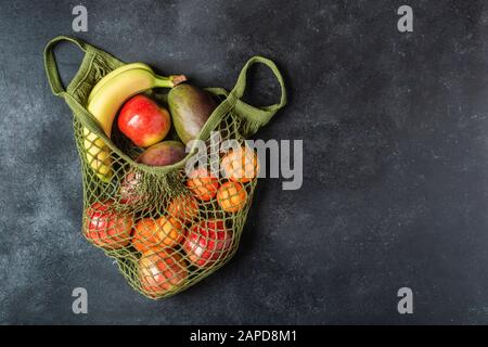 Fresh fruit in a green string bag on a black background. Bananas, apples, oranges, and mangoes.