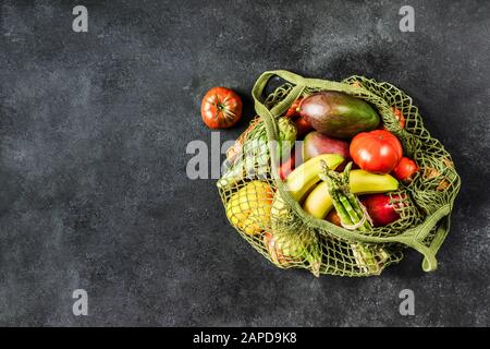 Fresh vegetables and fruits in a green string bag on a black background. No plastic, only natural materials and natural products. Stock Photo