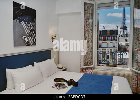 Window view of the Eiffel Tower from a Paris hotel room, Les Jardins d'Eiffel clean well made up bed, apartments, Paris roofs, blue sky Stock Photo