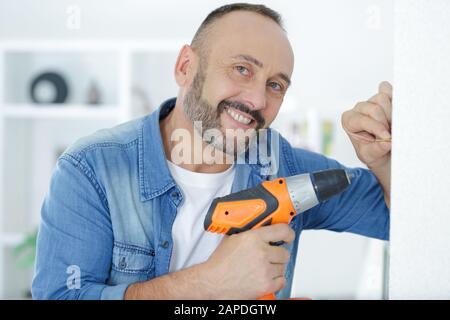 mid-adult man drilling hole in wall Stock Photo