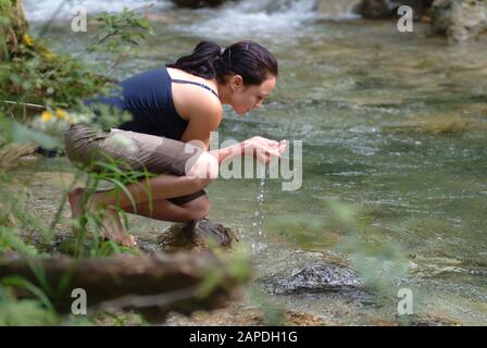 Junge Frau trinkt Wasser aus einem Bach - Young Woman drinking Water out of a River Stock Photo