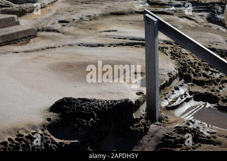 Carved steps on the rock shelf and a wooden handrail, a wet terrestrial moonscape leading down to Maroubra Ocean Pool Stock Photo