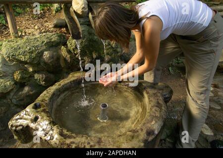 Junge Frau trinkt Wasser aus einem Brunnen - Young Woman drinking Water out of a Fountain Stock Photo