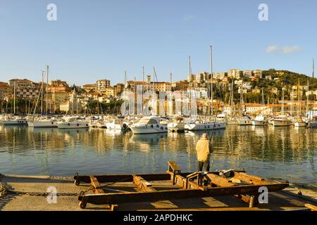 Scenic view of the harbor of Porto Maurizio in the Riviera of Flowers with an elderly fisherman fishing on a pier in a sunny winter day, Stock Photo