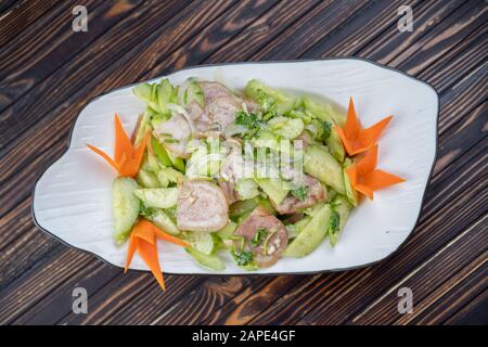 Typical Chinese salad of cucumbers and pork in a white plate on a wooden background Stock Photo
