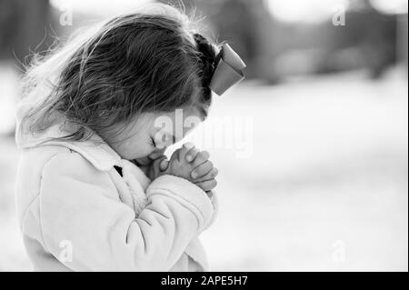 Greyscale of a little girl praying under sunlight with a blurry background Stock Photo