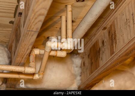Old PVC plastic water supply pipes installed under house in crawlspace. Hot and cold water plumbing system for bathroom sink and shower Stock Photo
