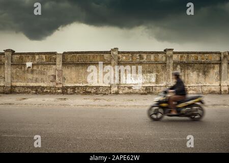 Fast-moving cool motorcycle riding moving left in a deserted part of a town under the gloomy sky Stock Photo