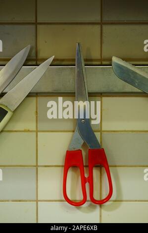 Vertical shot of red scissors attached to a magnet on a wall Stock Photo