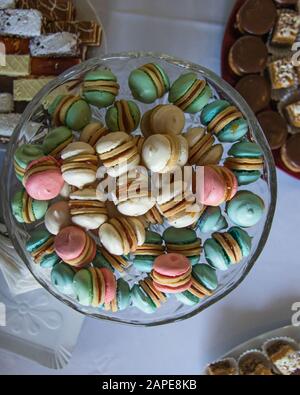 Close up shot of colorful macarons in a glass bowl with some desserts on the side Stock Photo
