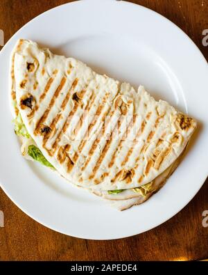 Flatbread Pita bread grilled panini sandwich folded in half with lettuce, turkey, melted cheese on a white plate top down Stock Photo