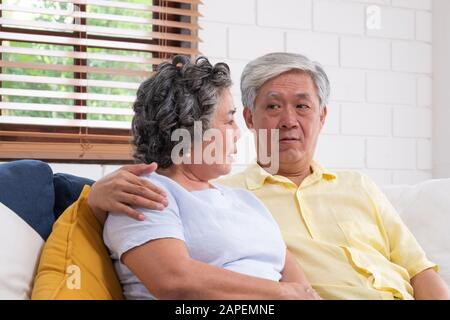 Asian couple senior embracing and sitting comfortably on sofa and  talking in living room at home. Stock Photo