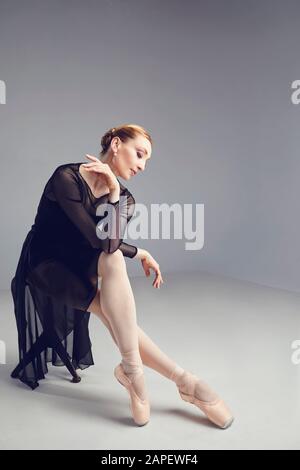 Dancer woman in black dress posing sitting on a chair Stock Photo