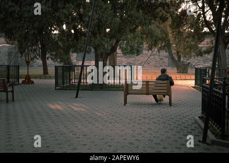 Young, lonely man seating along on a bench at sunset, in a park in Beijing, China, in winter, in the cold Stock Photo