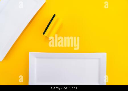 Cleaning yellow household sponge with white plate on a yellow background. Group of bright colored sponges for washing dishes. Cleaning equipment for k Stock Photo