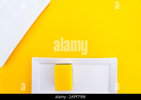Cleaning yellow household sponge with white plate on a yellow background. Group of bright colored sponges for washing dishes. Cleaning equipment for k Stock Photo