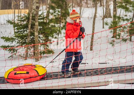 Boy with tubing rises on a travelator to the mountain. Child having fun on snow tube. Boy is riding a tubing. Winter fun for children Stock Photo