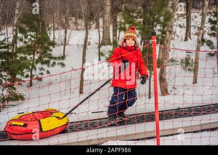 Boy with tubing rises on a travelator to the mountain. Child having fun on snow tube. Boy is riding a tubing. Winter fun for children Stock Photo