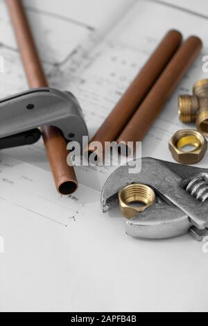 Copper pipe cutter and adjustable spanner wrench tools on a set of architecture building plans, with plumbing connectors.  Selective colour Stock Photo