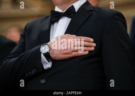 Details with a man in tuxedo holding his hand on his hearth while hearing the national anthem. Stock Photo