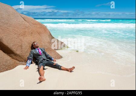 Survivor castaway businessman washed up on a tropical beach in a ragged torn suit Stock Photo